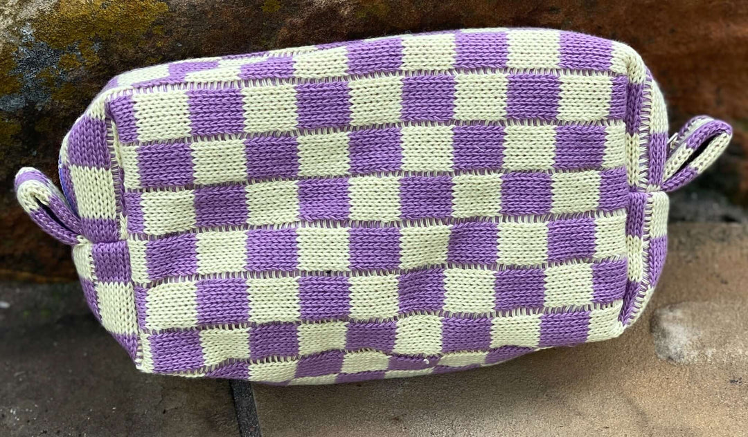A purple and light yellow checkered zipper pouch with a strap, placed on a textured surface.