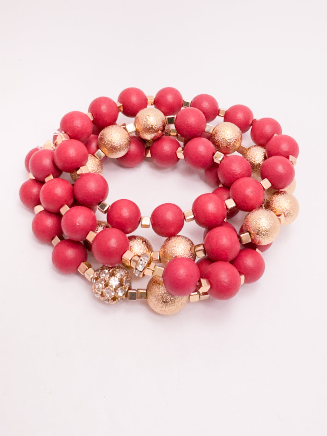 A set of stackable beaded bracelets with red and gold beads, featuring gold clasp.