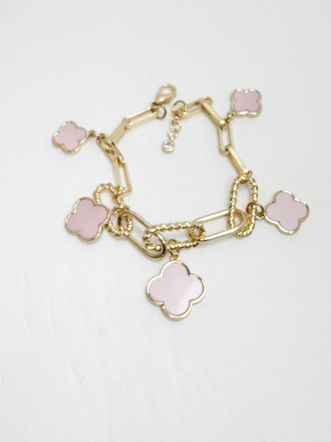 Gold bracelet with pink clover-shaped charms on a light gray background