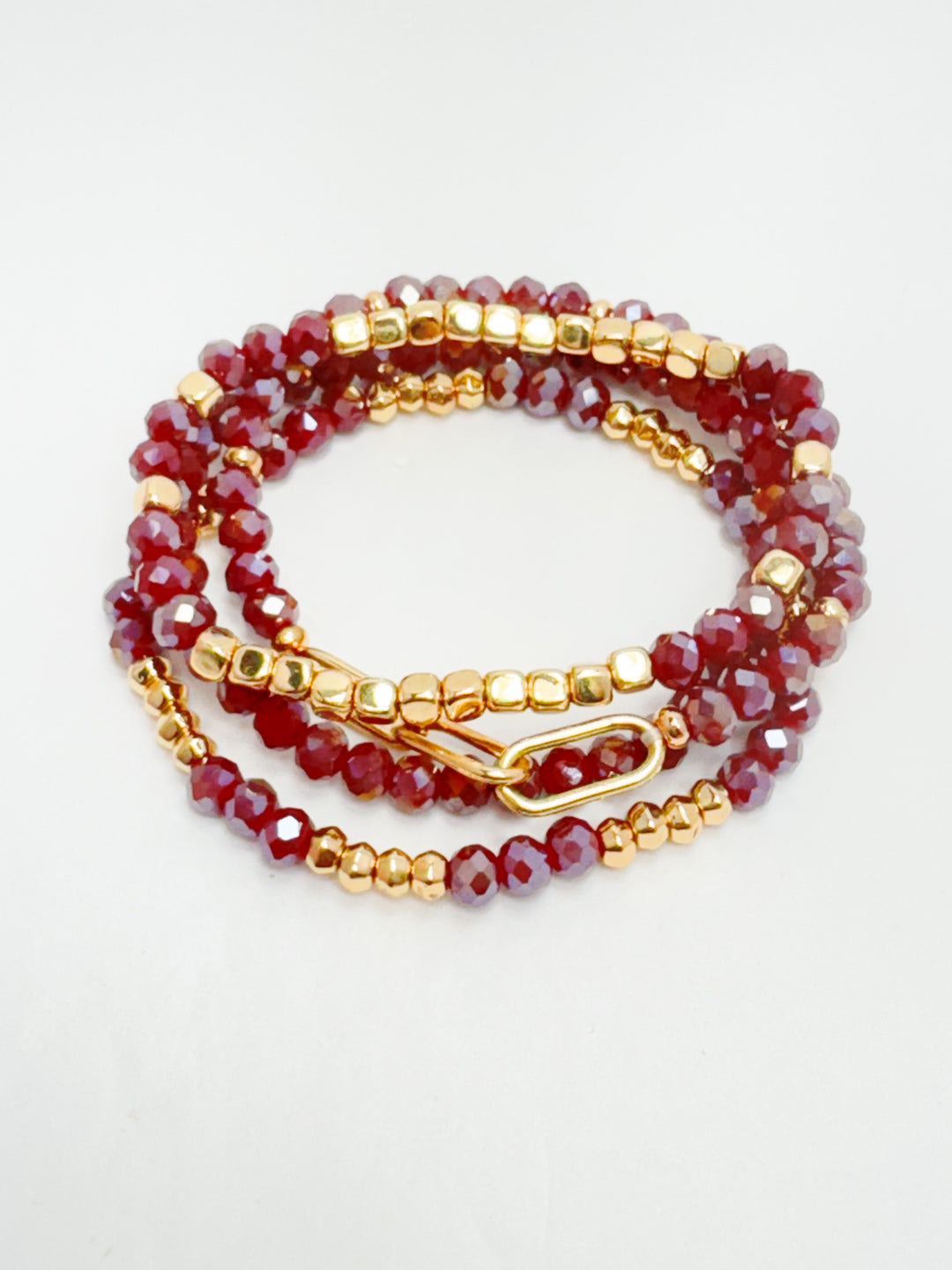 A set of stackable red beaded bracelets with gold accents.