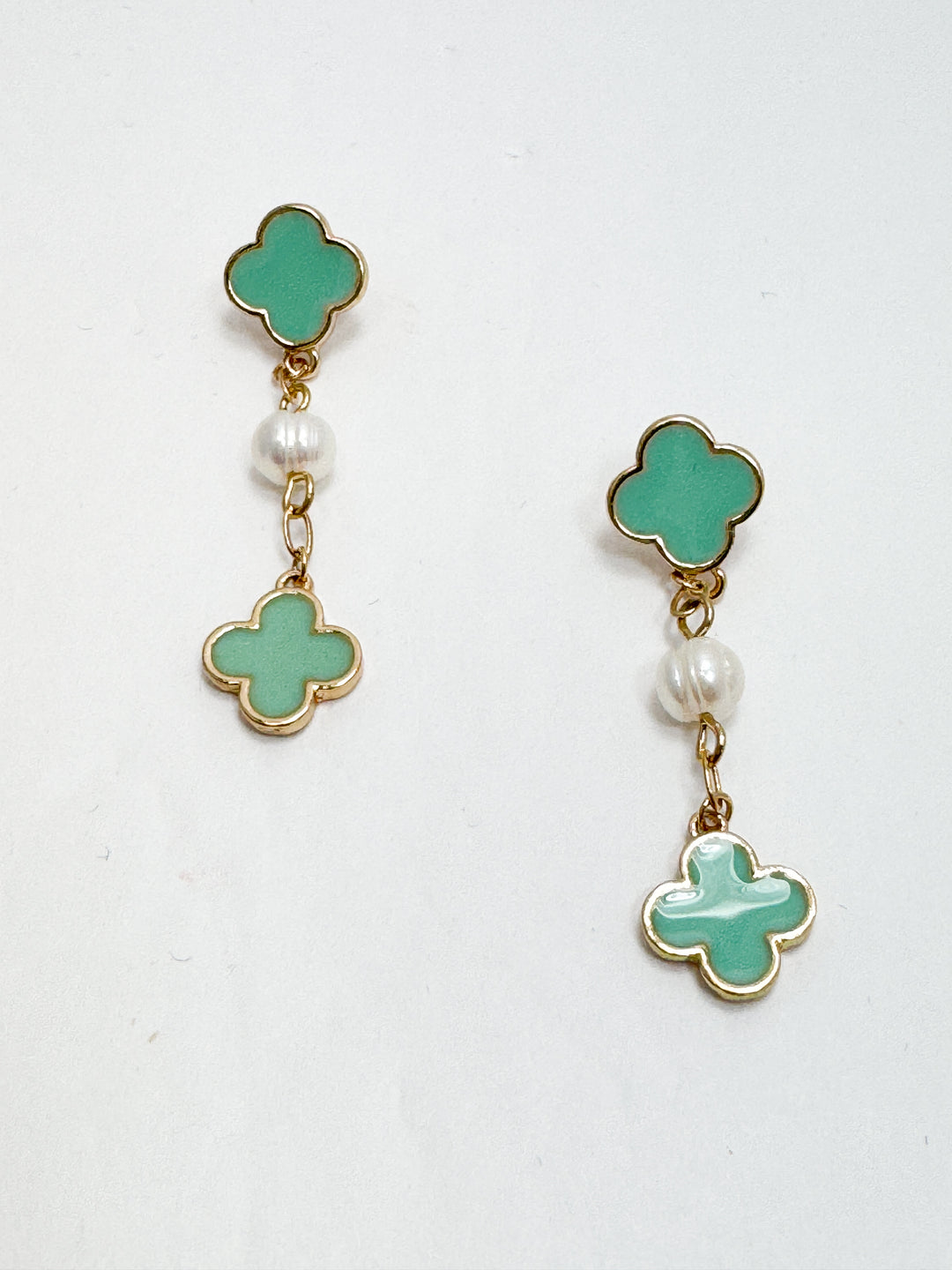 Pair of earrings with green clover-shaped drops and pearl-like beads on a white background