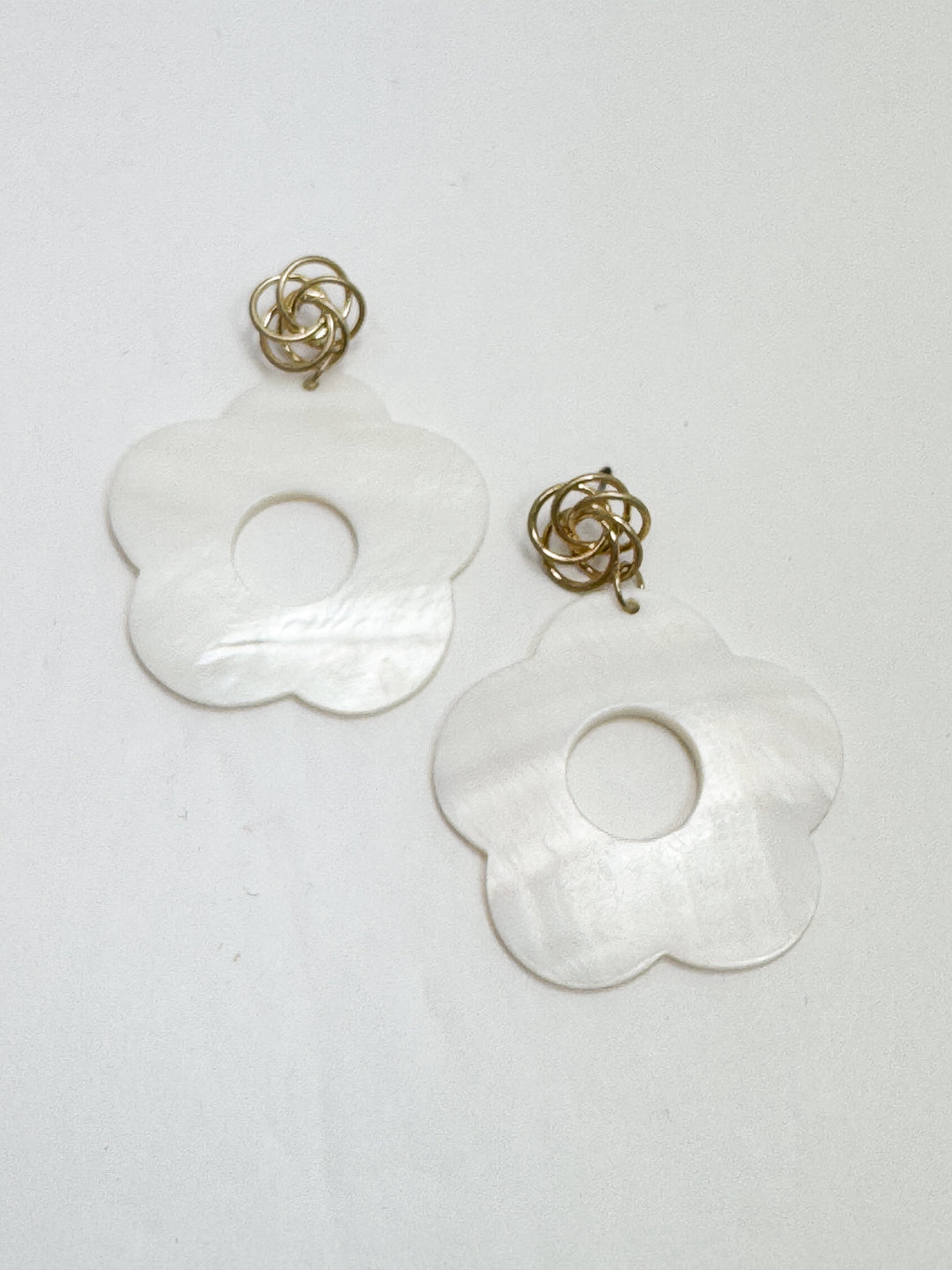 Pair of white floral earrings with gold accents on a light gray background
