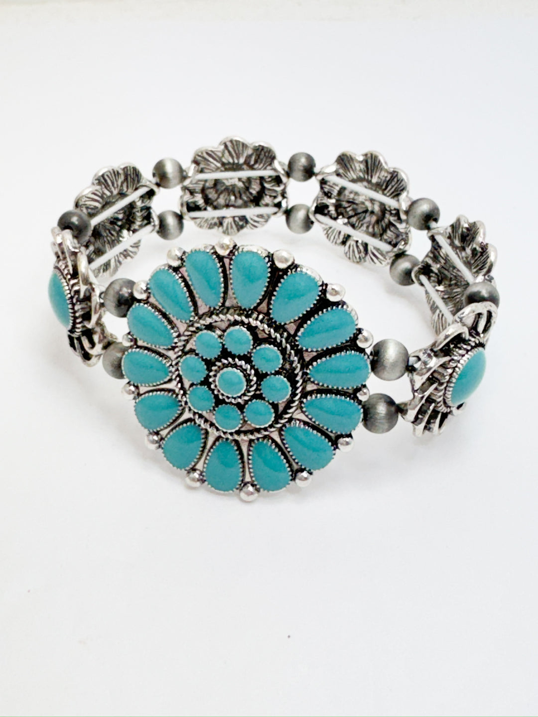 A stretchy bracelet with antique silver floral-style accents and a large turquoise embellished concho at the center.