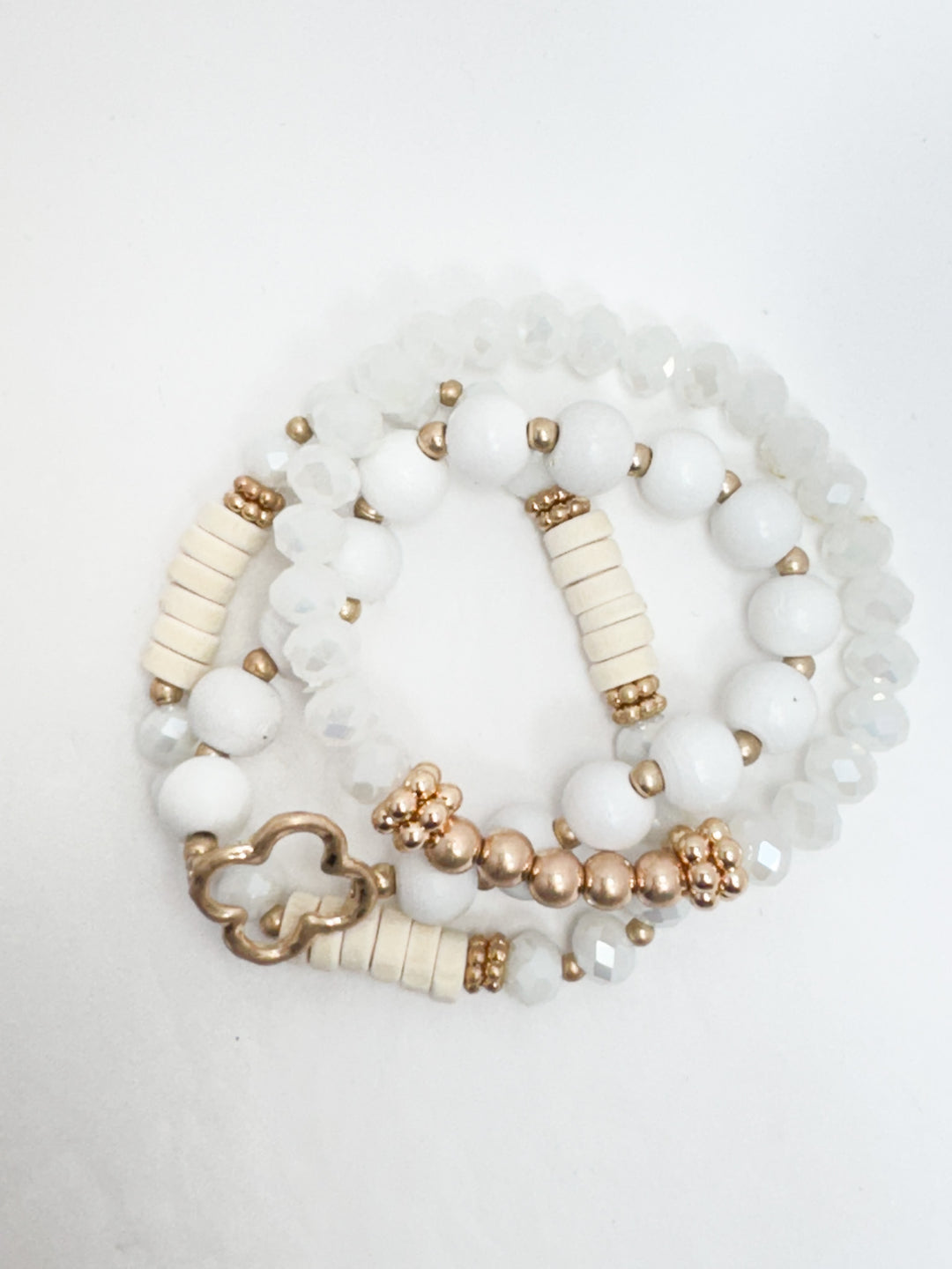 A set of layered clear and white beaded bracelets with gold accents.
