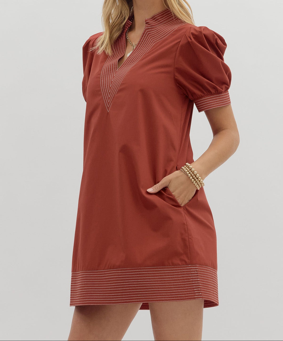 Woman wearing a rust-colored dress with puff sleeves on a light gray background
