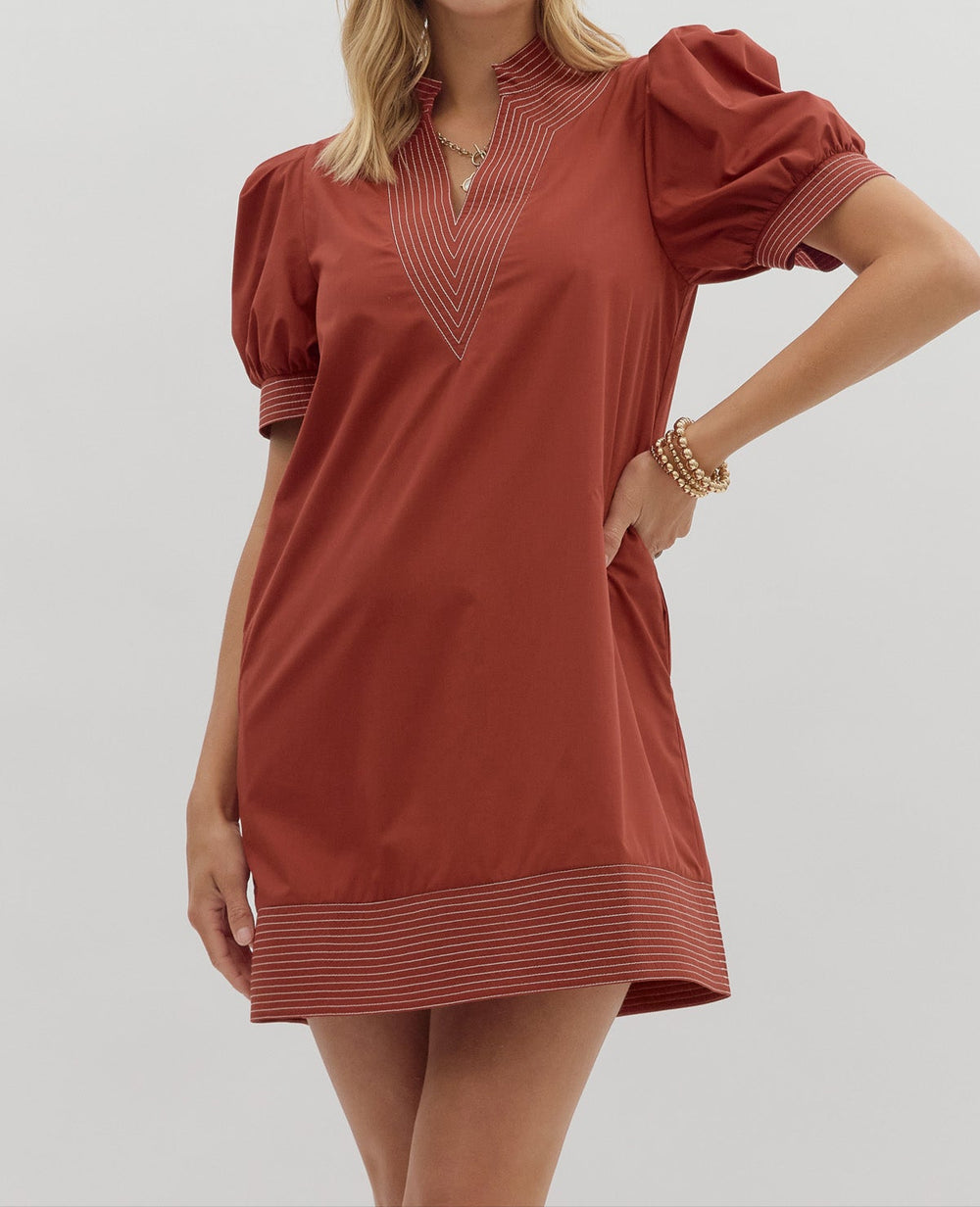 Woman wearing a rust-colored dress with puff sleeves on a light gray background