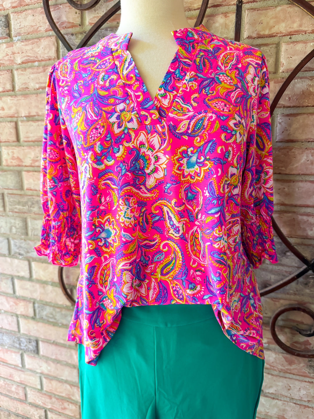 Colorful patterned blouse on a mannequin against a brick wall.
