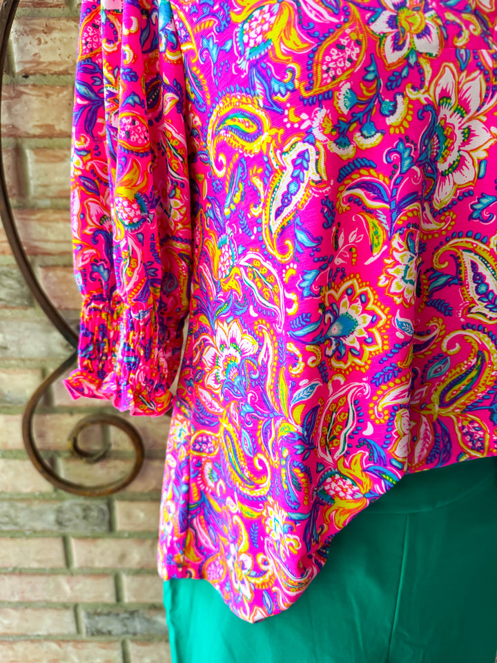 Colorful paisley patterned fabric draped over a chair against a brick wall.