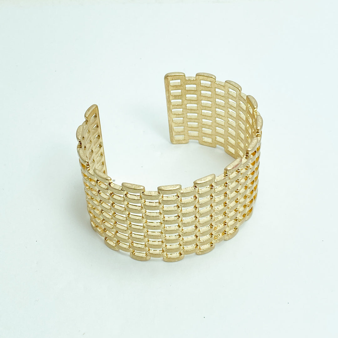 A gold-colored basket weave cuff bracelet on a white background