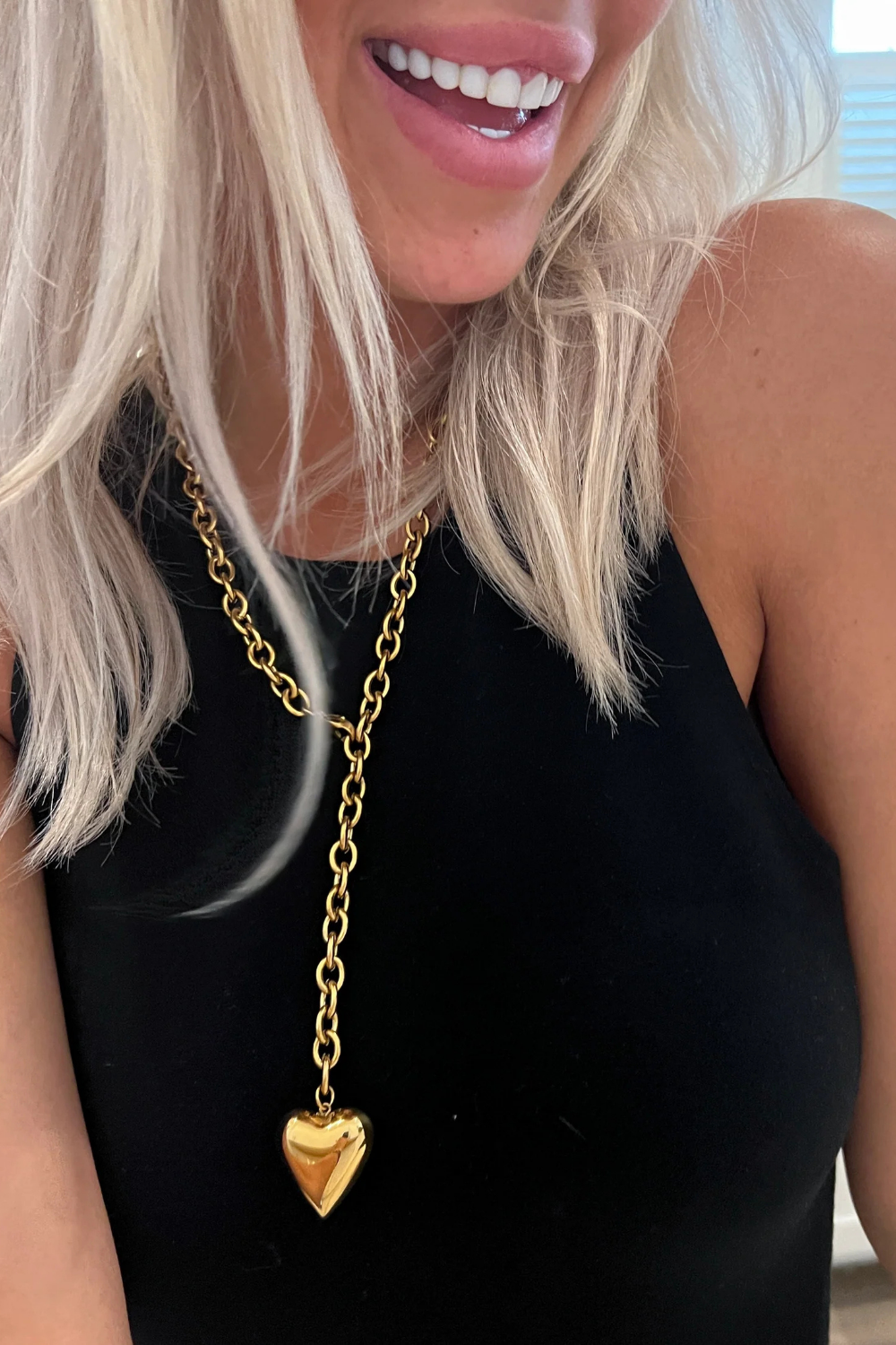 Woman wearing a black top and gold necklace with a heart pendant.