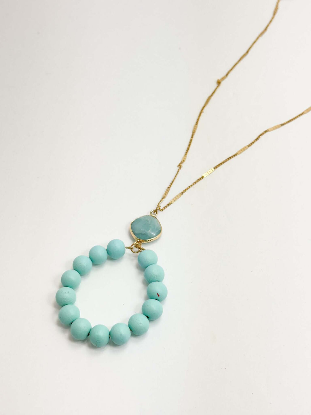 A long gold necklace with a turquoise circle pendant and additional turquoise beads.