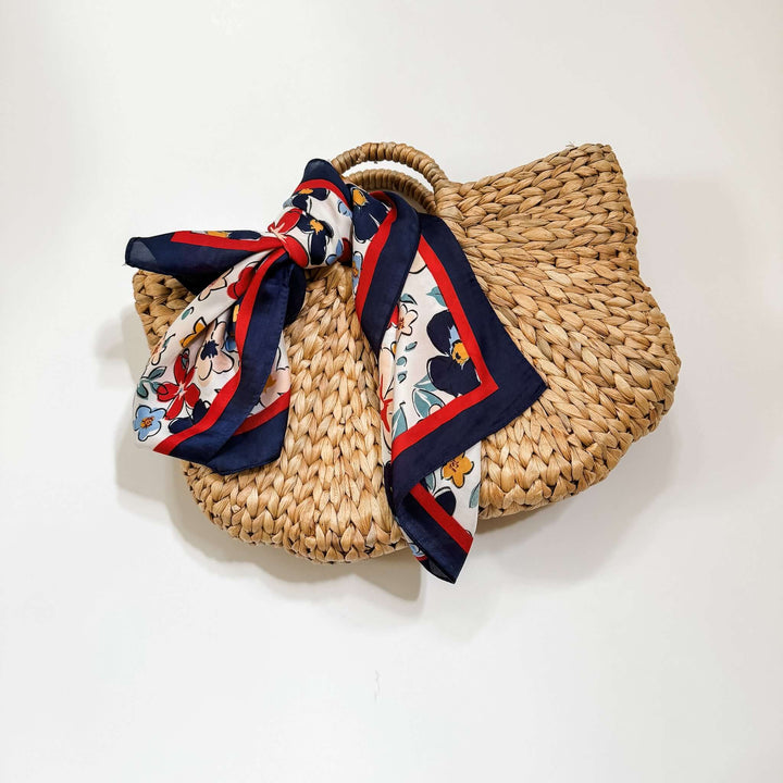A navy red and white floral scarf tied with a bow, displayed on a woven basket-like purse.