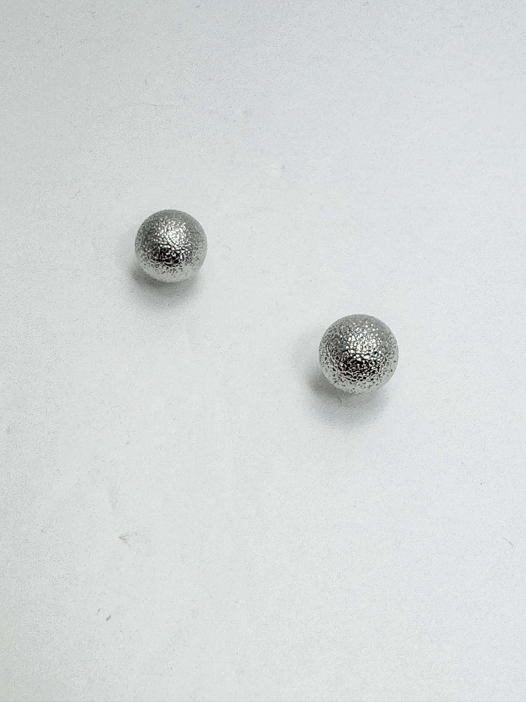 Two silver textured ball post earrings on a white background.