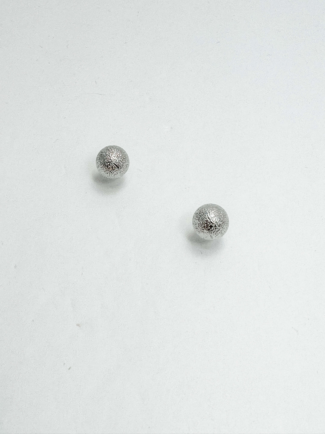 A pair of silver textured ball post earrings on a white background.