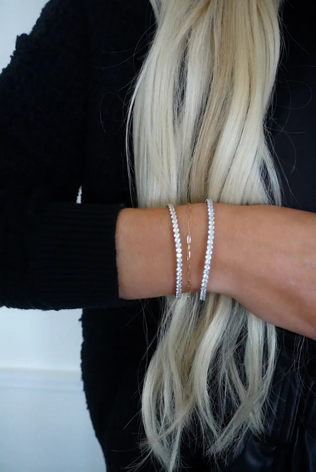 Person wearing two silver bracelets on a plain background