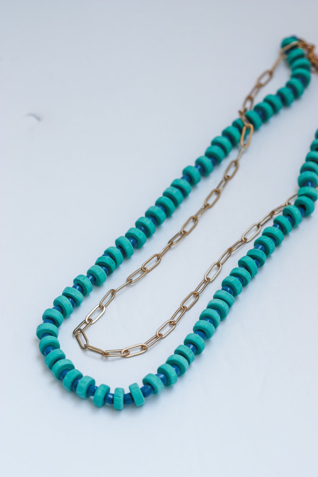 Turquoise beaded necklace with gold chain on a white background