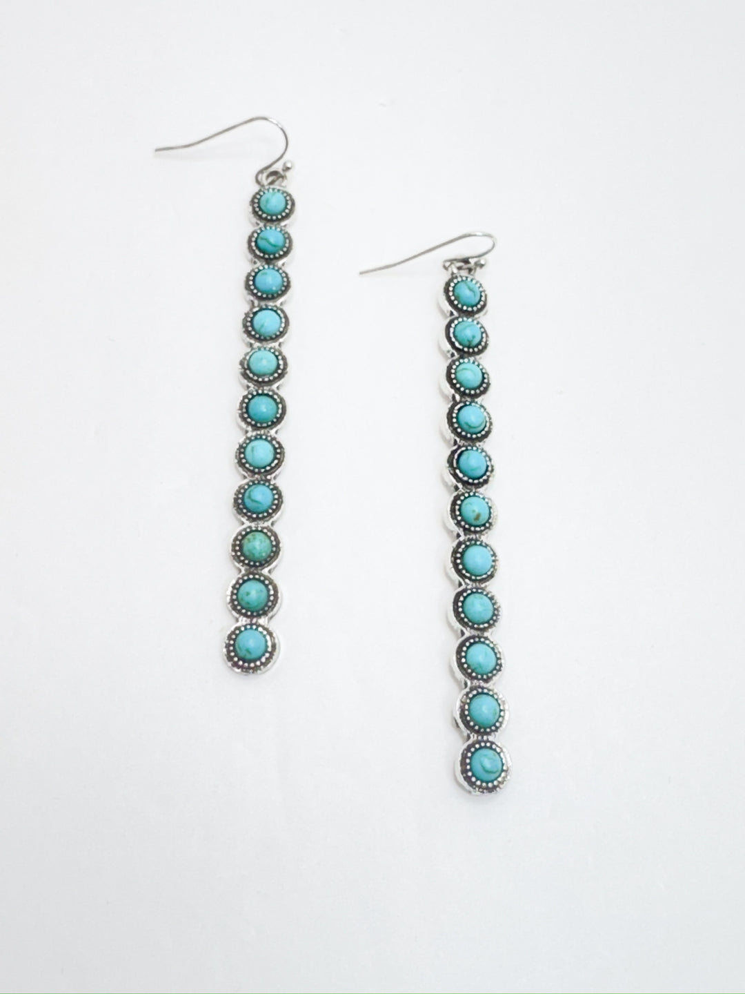 A pair of dangling earrings featuring stacked turquoise beads with silver surrounding on a white background