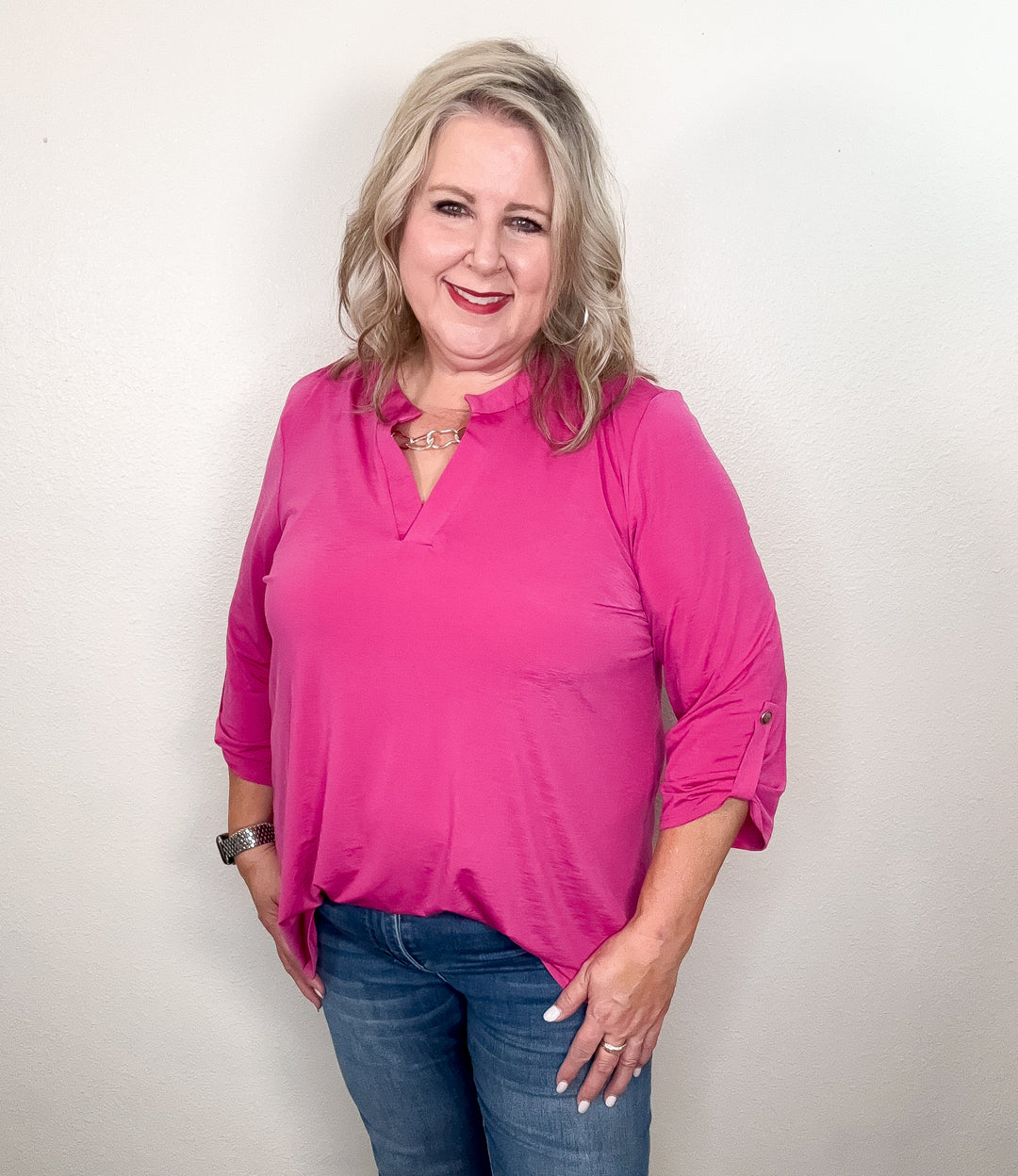 A person wearing a pink top with a notch neckline and 3/4 length sleeves with tab detail, paired with jeans.