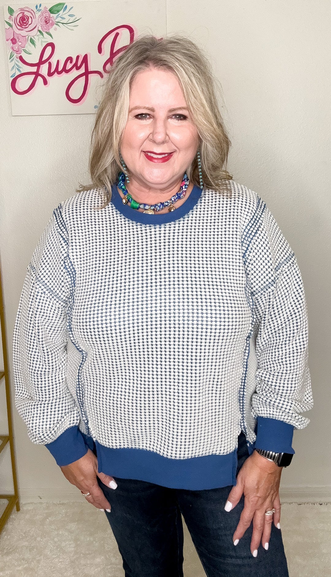Woman wearing a checkered sweater with blue accents in front of a branded backdrop