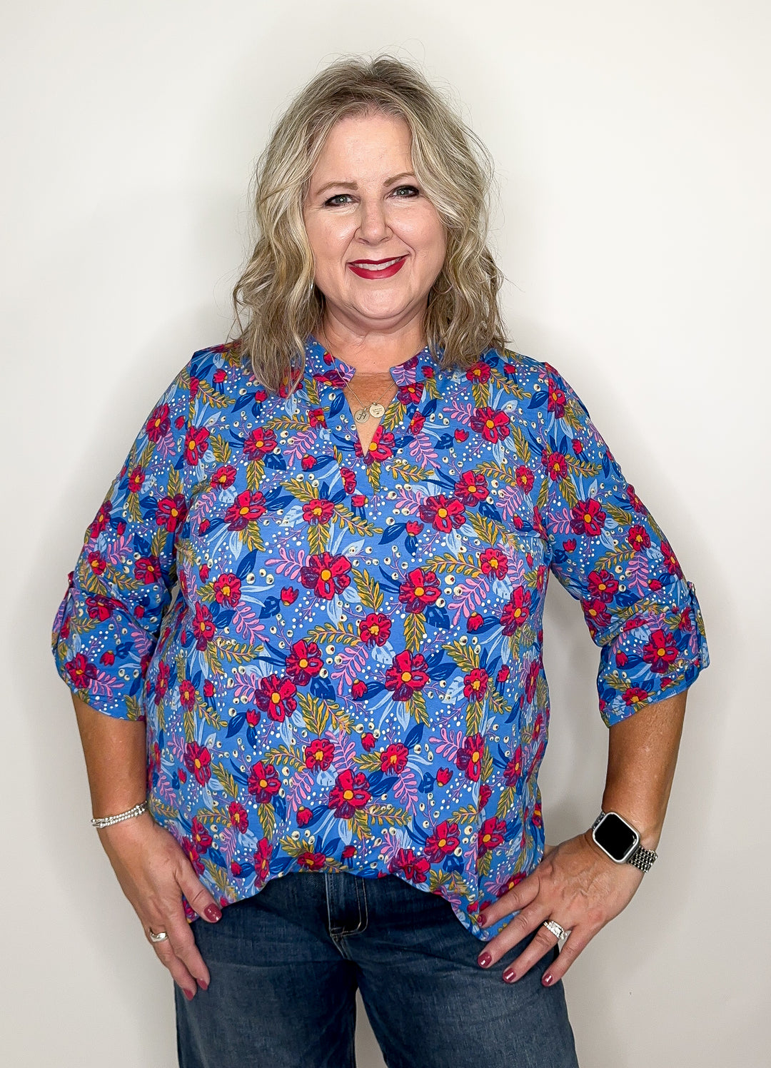 A person wearing a vibrant, multicolored floral top with a notched collar and 3/4 sleeves, paired with jeans.