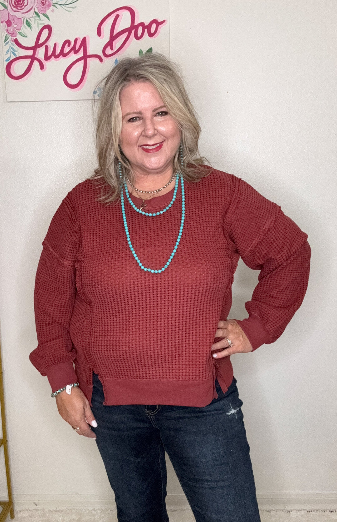Woman wearing a red sweater and blue jeans with a 'Lucy Doo' sign in the background
