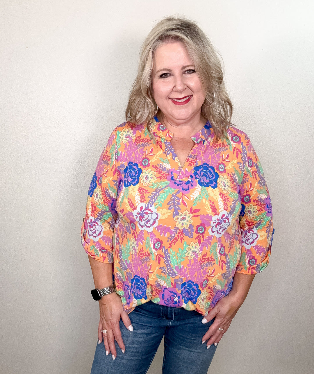 A woman wearing a floral top with a mix of peach, blue, purple, and mint colors