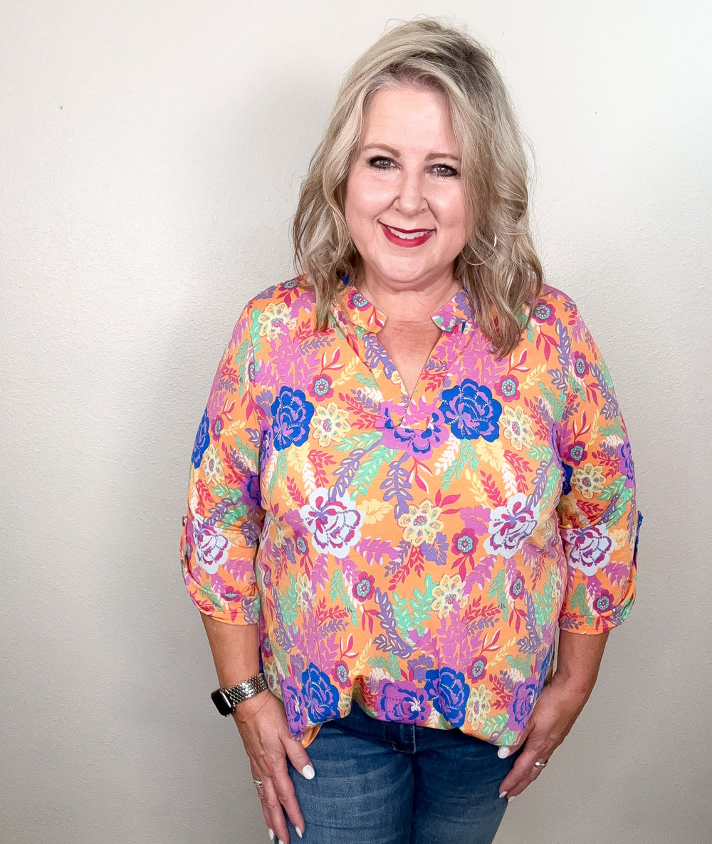 A woman wearing a floral top with a mix of peach, blue, purple, and mint colors