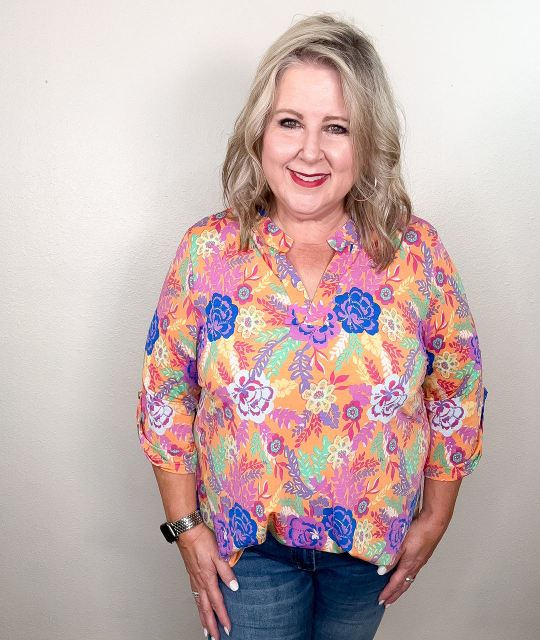 A woman wearing a floral top with a mix of peach, blue, purple, and mint colors