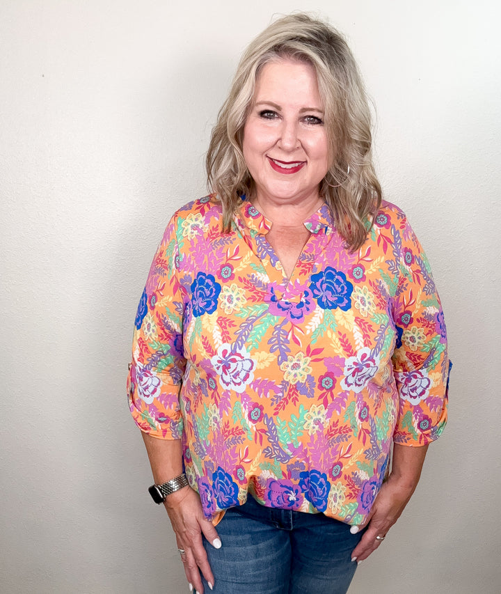 A woman wearing a floral top with a mix of peach, blue, purple, and mint colors