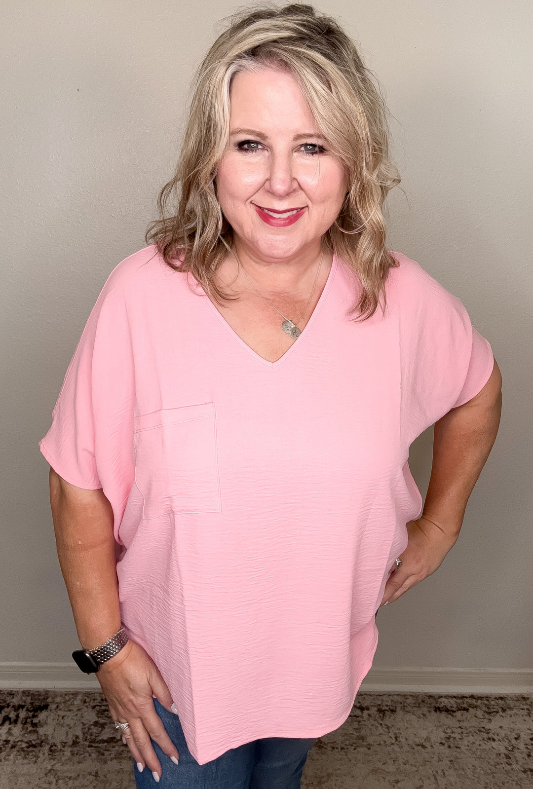 A person wearing a blush pink airflow top and blue jeans, standing against a neutral background.