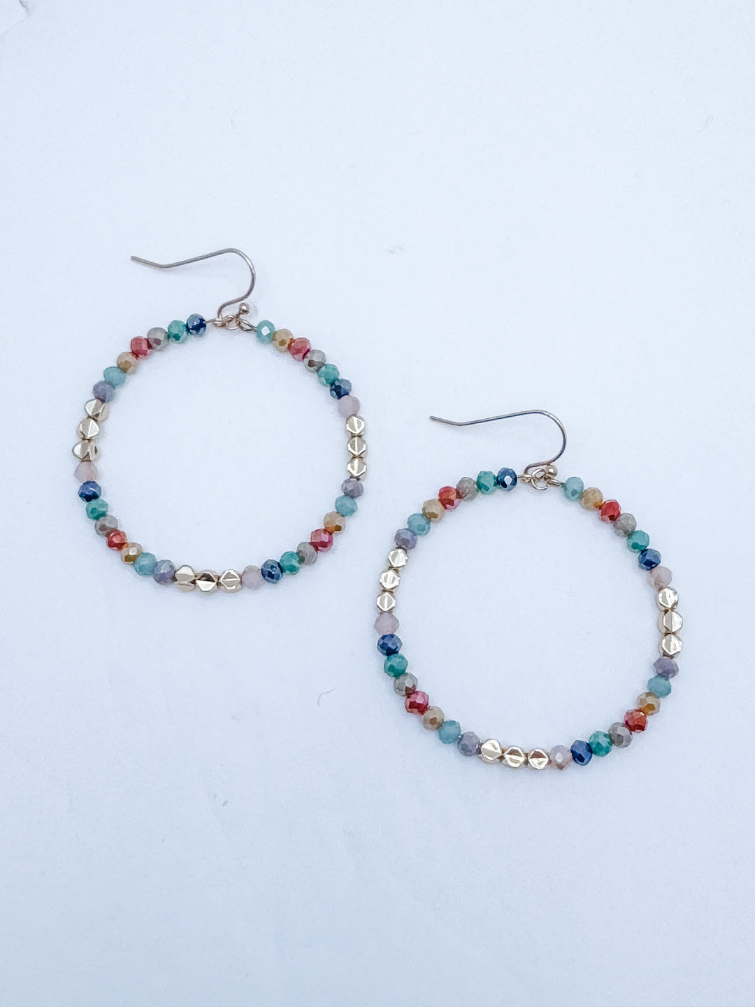 Multicolored beaded hoop earrings on a light blue background