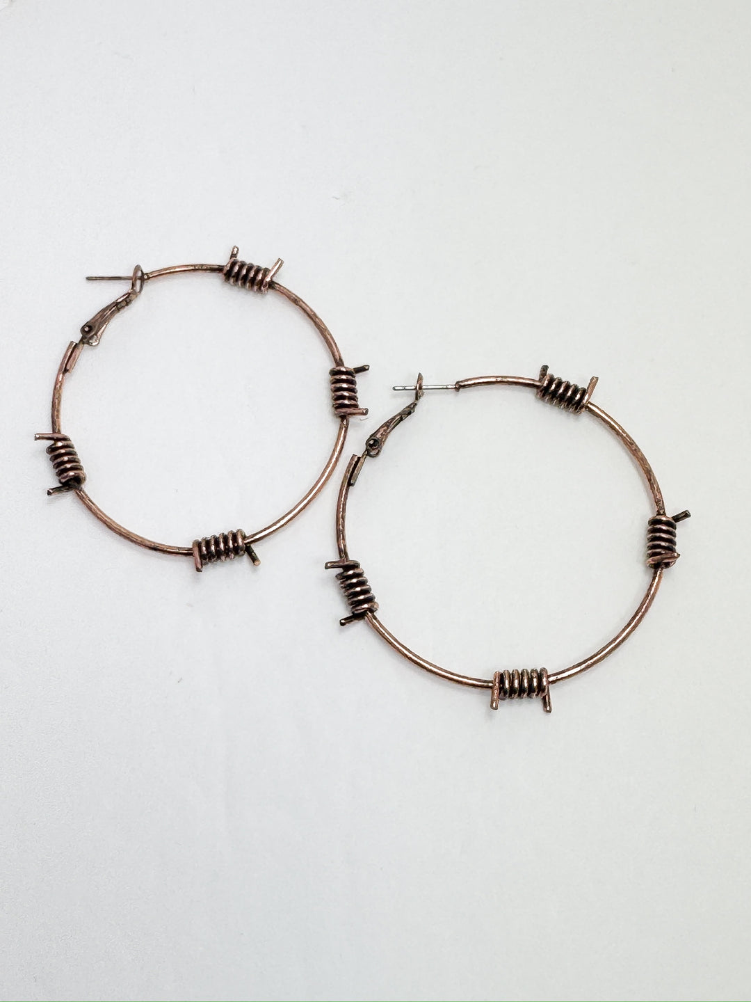 A pair of copper-colored hoop earrings with a barbed wire pattern on a white background.