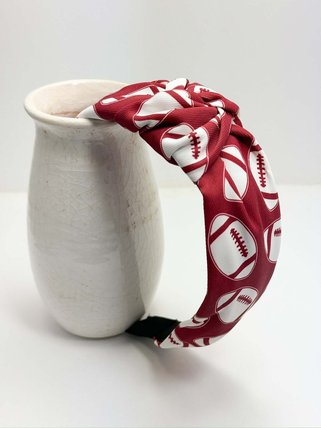 A headband with a crimson and white football pattern, wrapped around a beige ceramic vase.