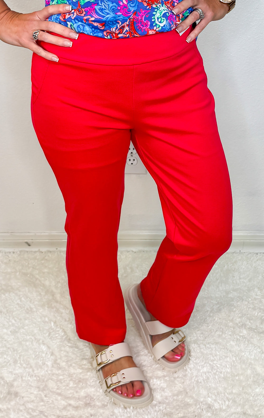 A model wearing high-waisted red straight leg pants with a floral top and white sandals.