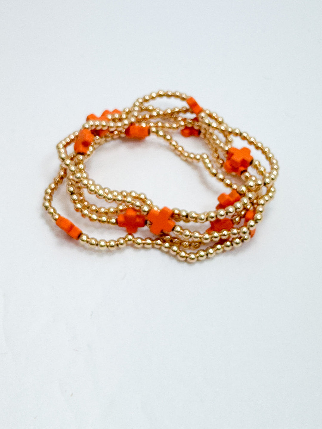Gold beaded bracelets with orange beads on a white background