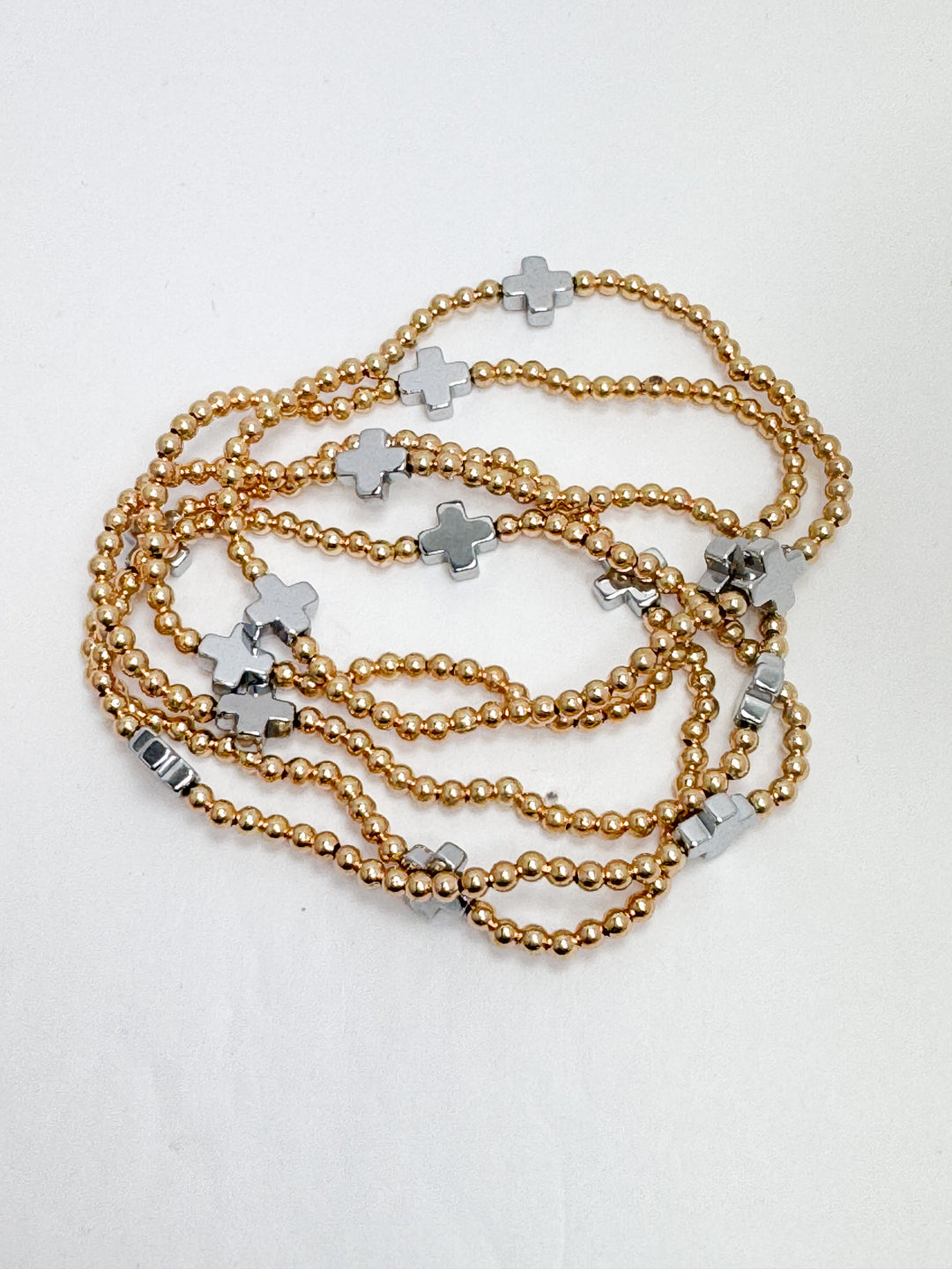 A gold beaded bracelet with silver cross accents laid out on a surface.