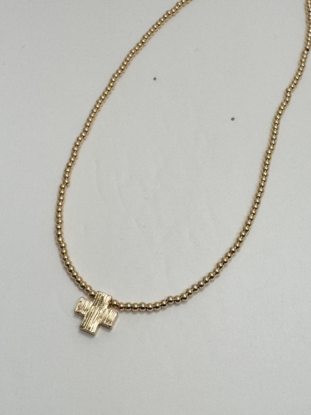 Gold necklace with a small pendant on a light gray background
