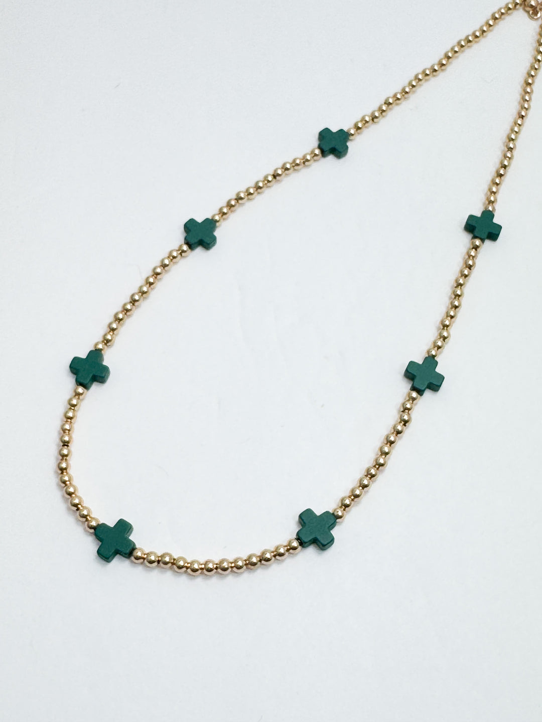 Necklace with green clover-shaped pendants on a gold chain against a white background