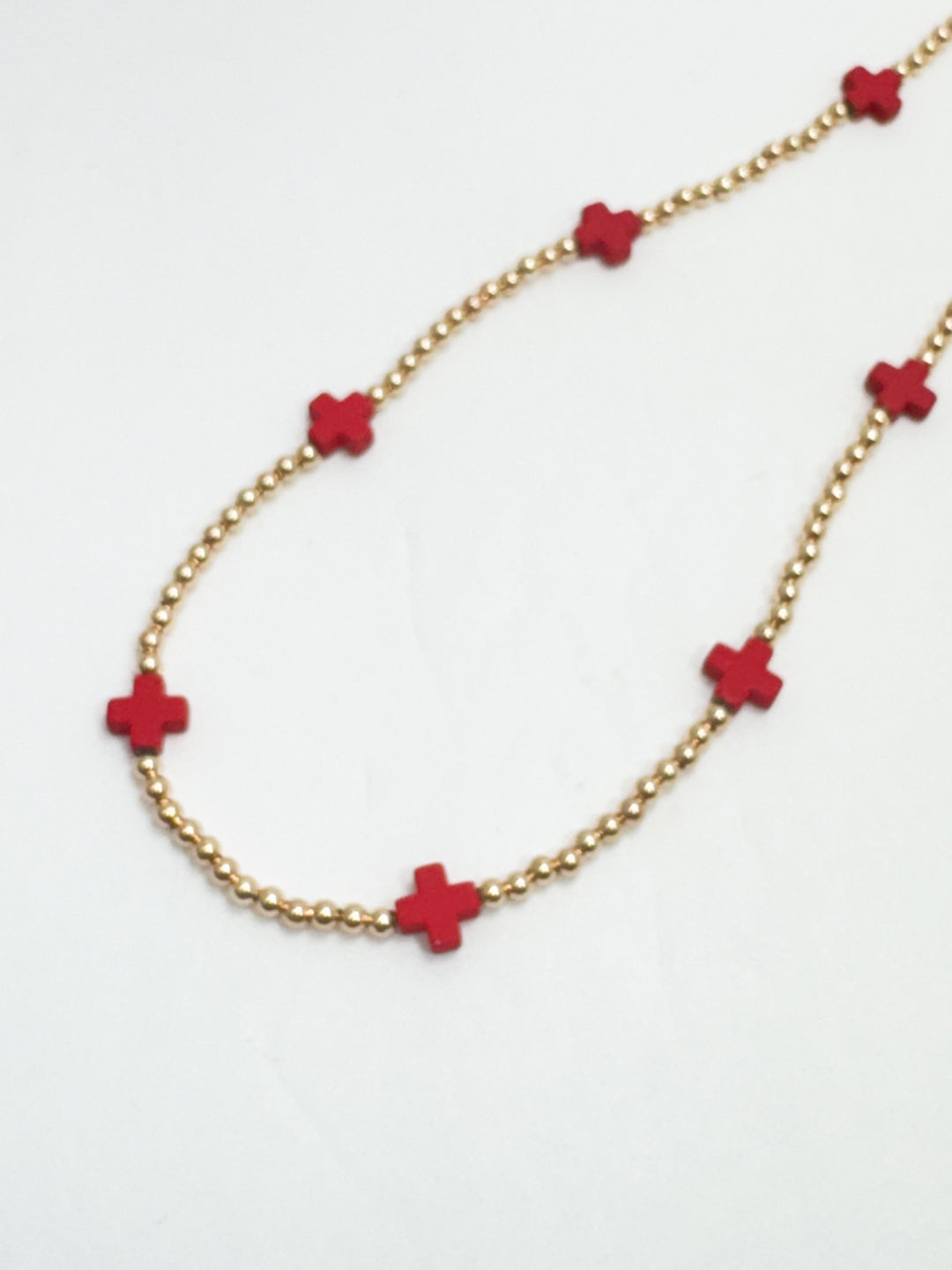 Necklace with red flower-shaped beads on a gold chain against a white background
