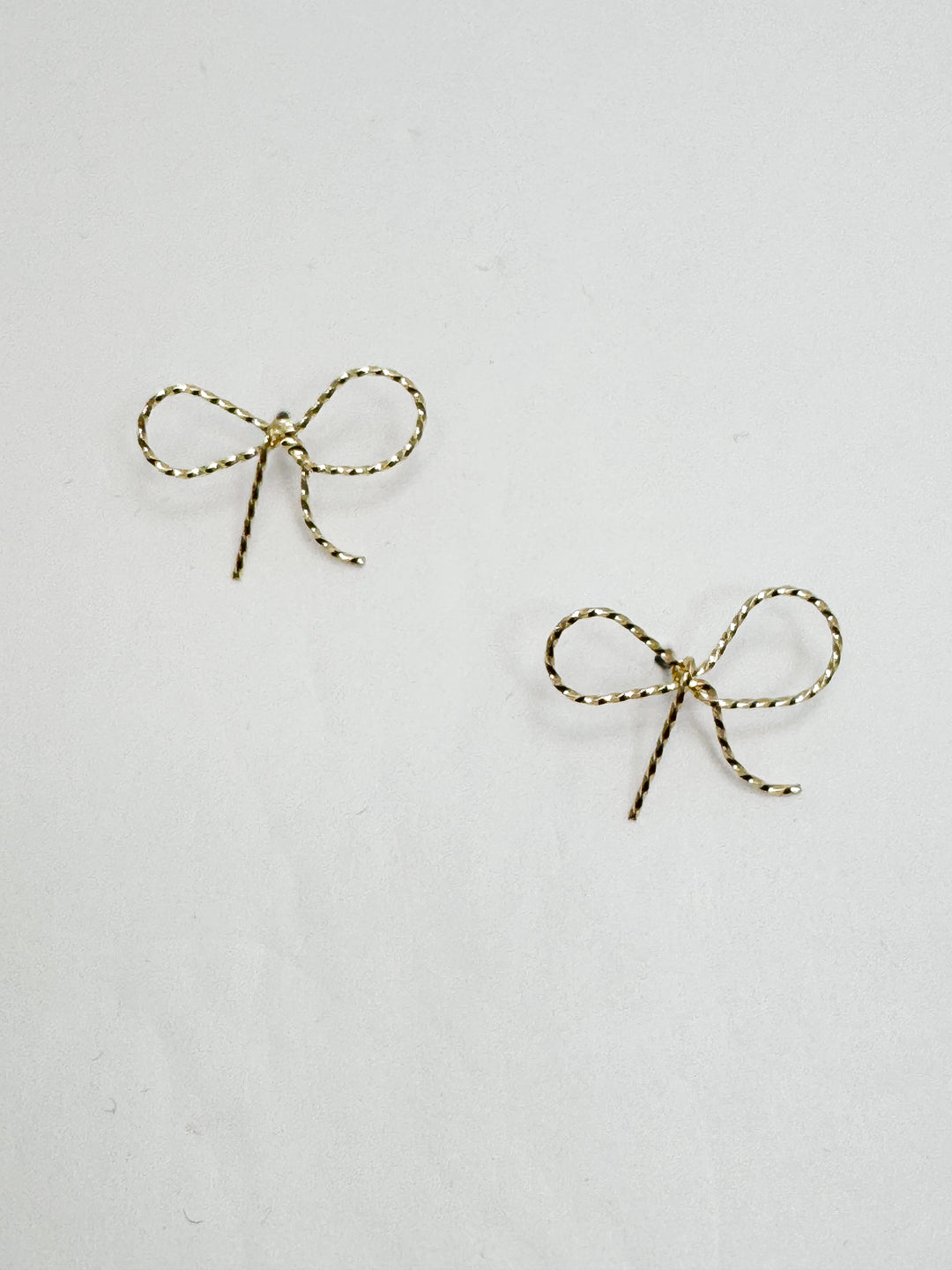 Pair of gold bow-shaped earrings on a light gray background