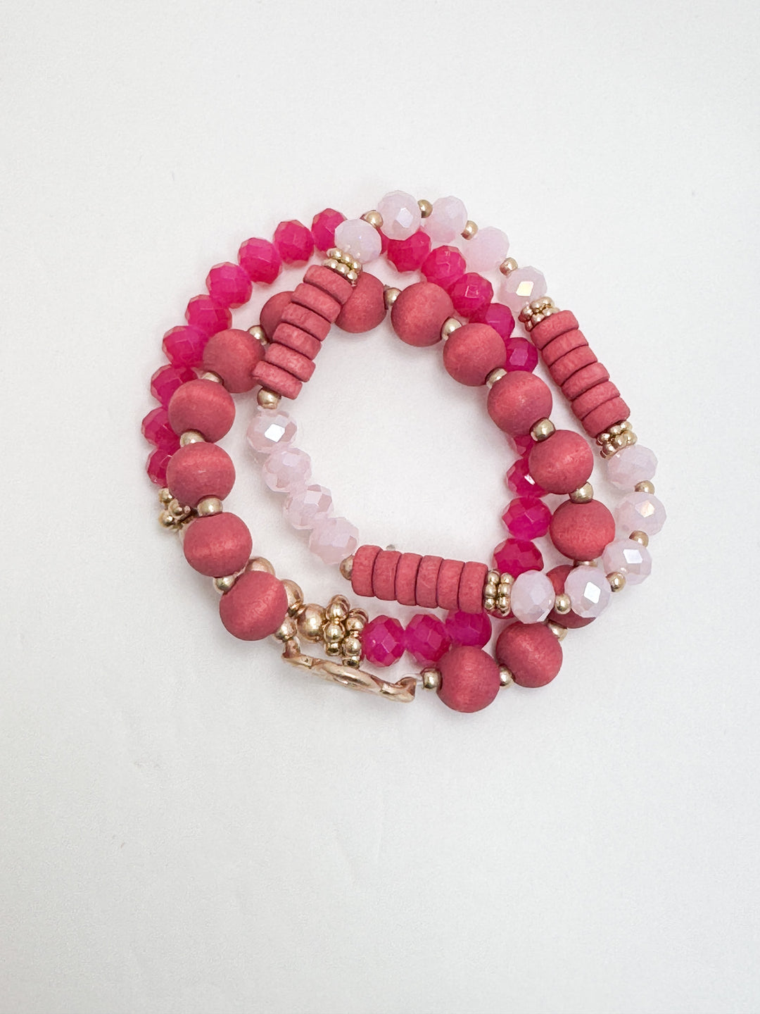 A set of stackable beaded bracelets in hot pink, light pink, and gold colors with textured and smooth beads.