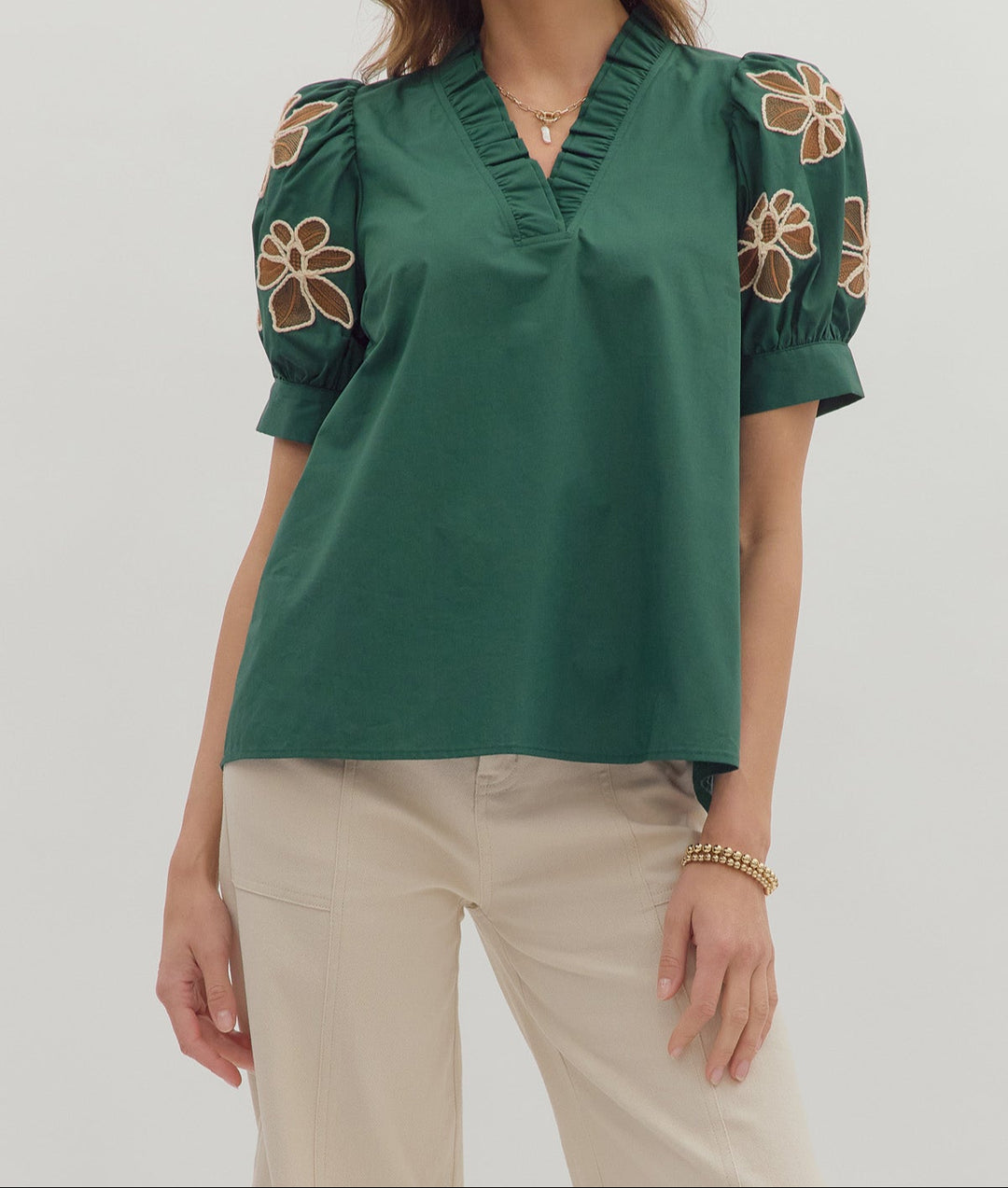 Woman wearing a green blouse with floral embroidery on sleeves against a white background