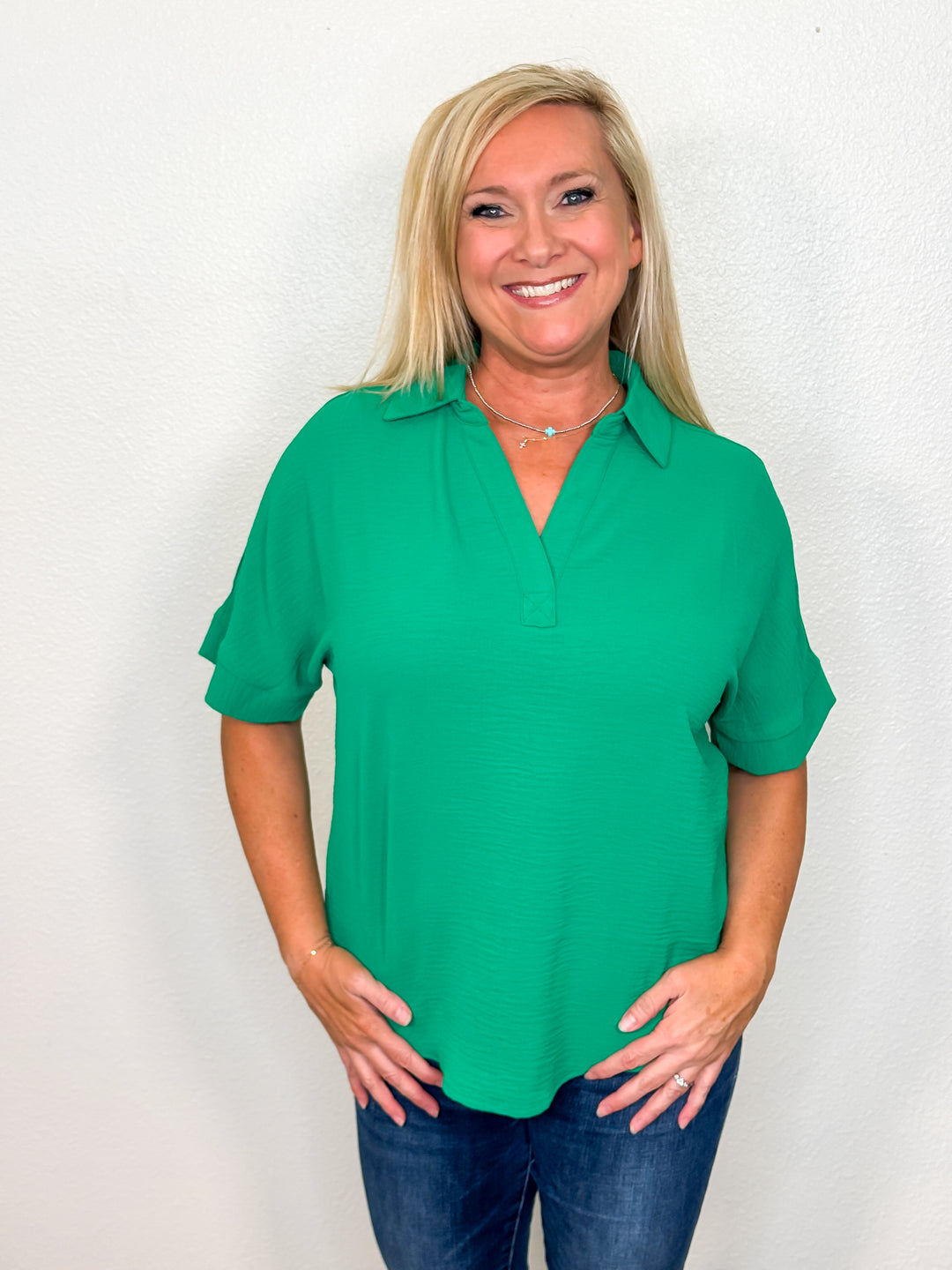 A woman wearing a collared V-neckline kelly green top with short sleeves, paired with jeans.