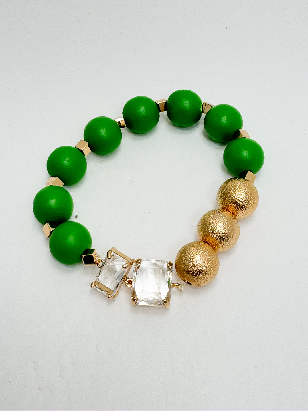 A bracelet featuring a mix of green painted wooden beads, gold beaded accents, and clear beads, with a gold-colored clasp.