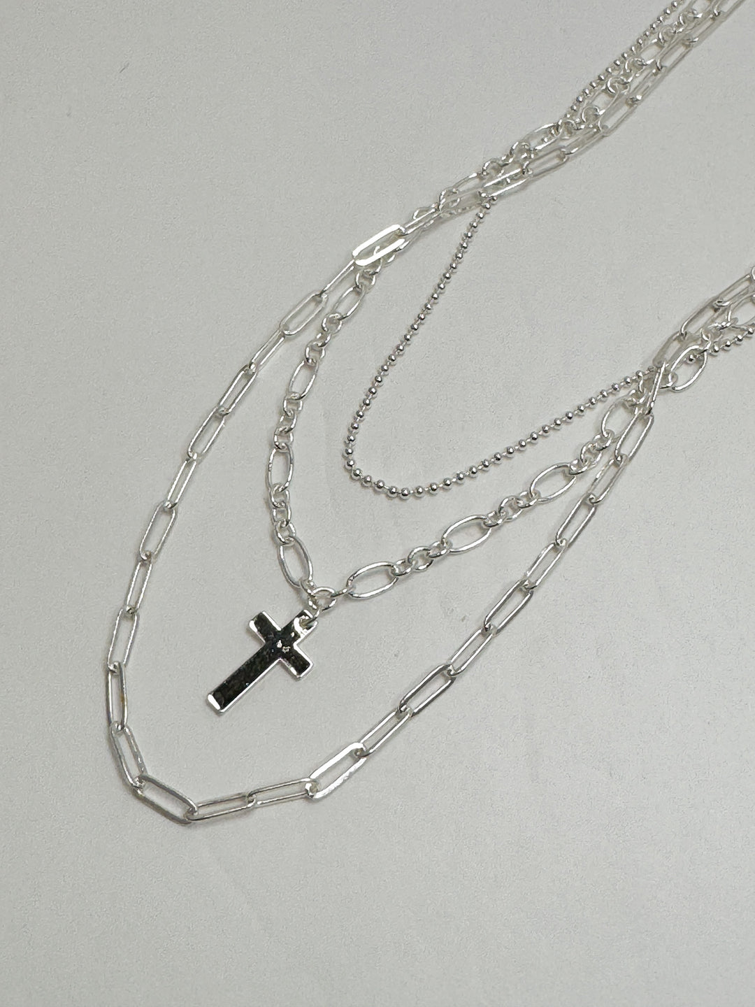 Silver chain necklace with a cross pendant on a light gray background