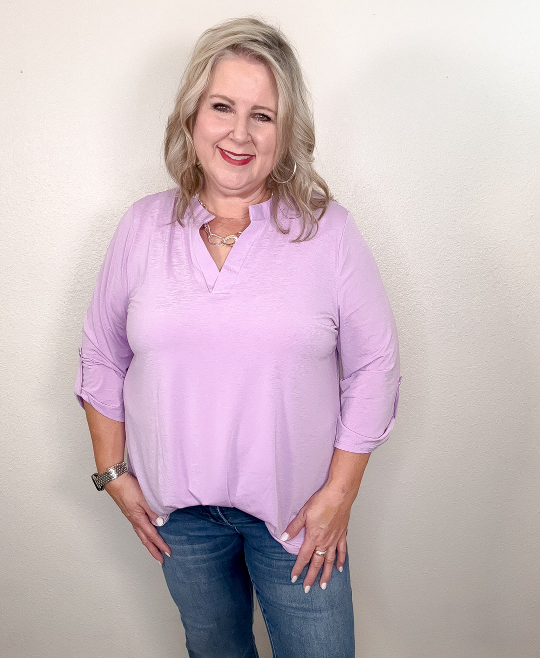 A woman smiling and wearing a long-sleeved purple top with a V-neckline.