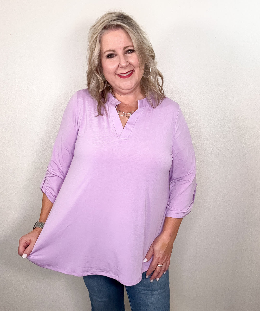 woman wearing a lilac colored top on a white wall