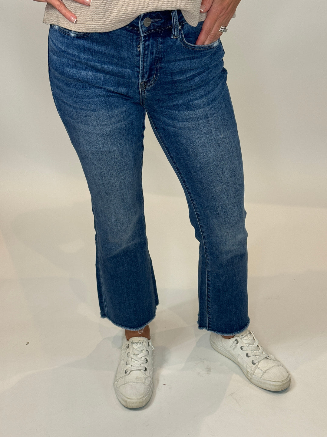 A person wearing a mid-rise crop boot cut blue denim jeans and white sneakers.