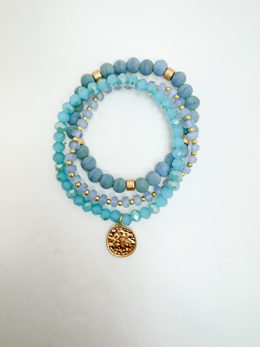 A set of three blue beaded bracelets with gold coin charm on a white background