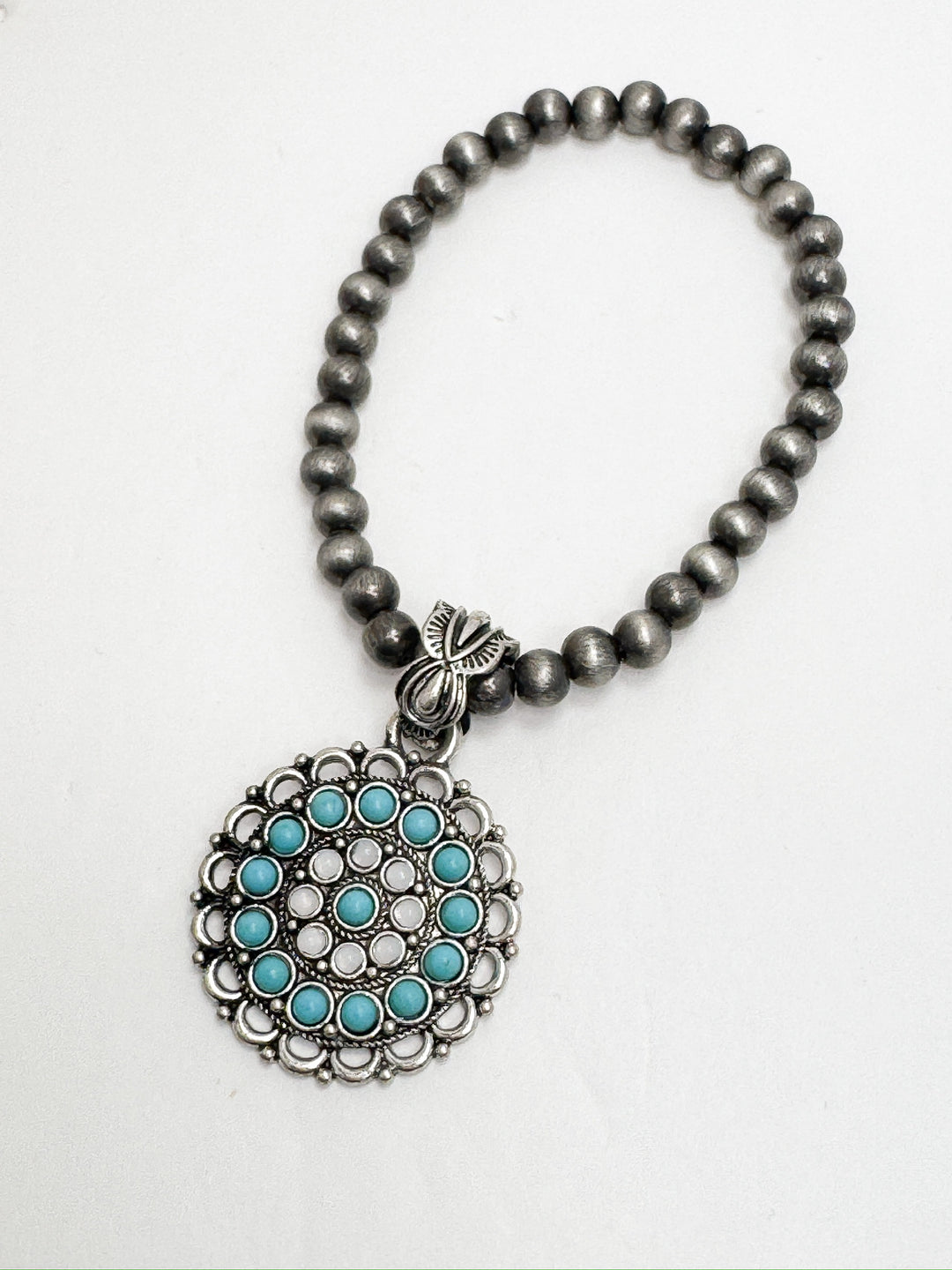 A stretchy bracelet with faux Navajo pearls and a circular concho pendant featuring turquoise and white beads.
